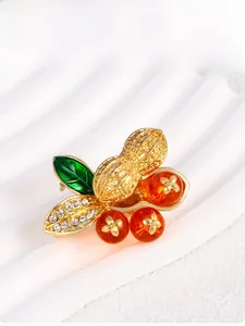 Macro shot of gold peanut brooch with orange beads and green enamel leaves