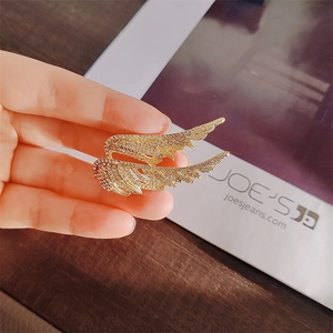 Macro shot of gold angel wing brooch with white rhinestones held by hand for scale
