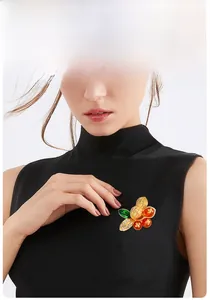 Detail of peanut-shaped brooch with golden finish and orange beads on black fabric