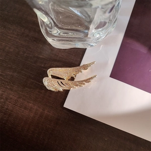 Detailed close-up of golden angel wing brooch with sparkling rhinestones and metal texture