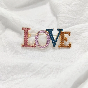 Goldene LOVE Buchstaben Brosche mit bunten Strasssteinen auf weißem Leinenhintergrund
