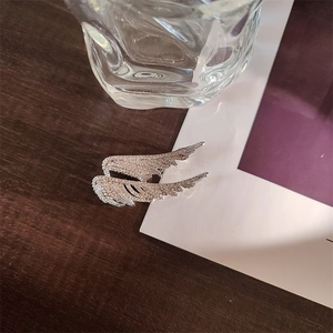 Macro detail of silver angel wing brooch with sparkling white zircons on wooden surface