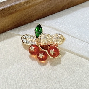 Macro detail of peanut brooch with white crystals and red beads on white fabric