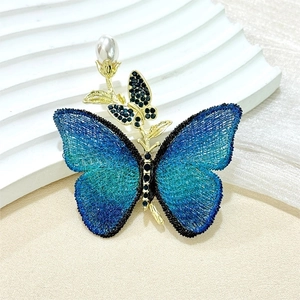 Broche papillon brodée bleue vintage avec perle et détails dorés sur support d'exposition