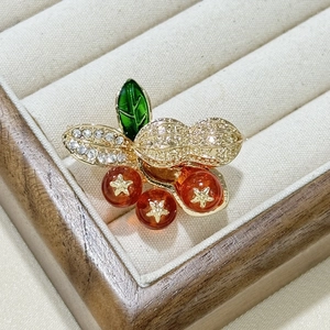 Close-up of a golden peanut brooch with sparkling white stones and orange resin fruits