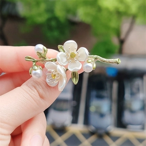 Elegant jasmine flower brooch with white petals and pearls held against an outdoor background