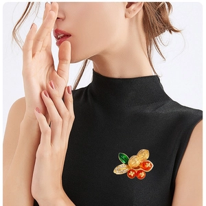 Peanut and persimmon brooch with red enamel and crystals on a black sweater