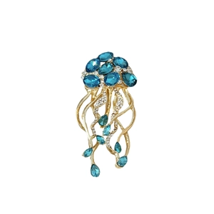 Broche méduse artistique avec monture dorée et gemmes bleues en gouttes sur fond blanc
