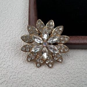 Detalle macro de un elegante broche de flor de pedrería con pétalos y gemas en aleación dorada