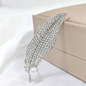 Elegant silver feather brooch with sparkling crystals and a white pearl on white silk