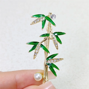 Detailed view of bamboo brooch with green enamel leaves, crystals and a pearl accent