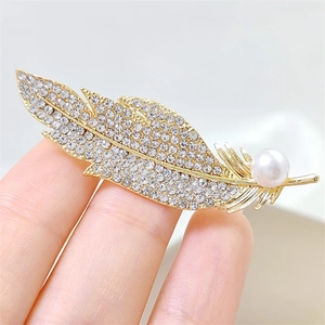 Macro detail of luxury gold feather brooch featuring white rhinestones and a single pearl
