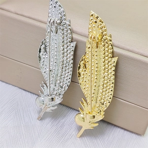 Macro detail of gold and silver feather brooches showing the back needle and metal texture