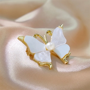 Elegant gold butterfly brooch with mother-of-pearl wings and a pearl center on silk fabric