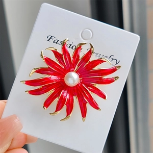 Gros plan d'une broche tournesol en émail rouge avec perle blanche sur carte de bijoux