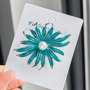 Détail d'une broche tournesol en émail turquoise avec une perle blanche sur sa carte