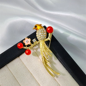 Elegant Chinese bird brooch with crystals and red pearls on a white silk background