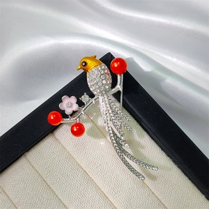 Detailed close-up of bird brooch with white rhinestones and red imitation pearls