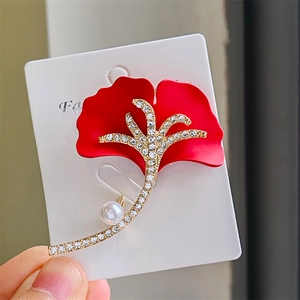 Détail d'une broche feuille de ginkgo avec pétales rouges, tige dorée et strass brillants