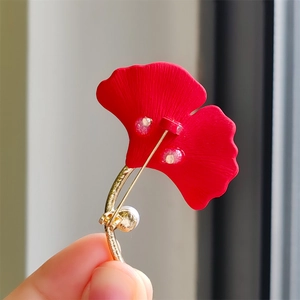 Détail macro d'une broche feuille de ginkgo rouge mat avec tige dorée et perle