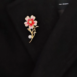 Detail einer eleganten roten Blumenbrosche mit Perle und Kristall am Revers