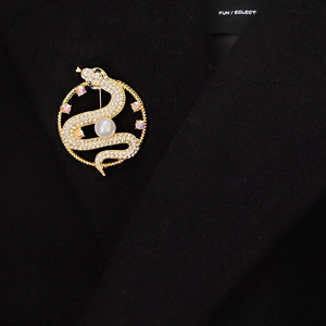 Detailed close-up of a golden snake brooch with white pearl and sparkling crystals