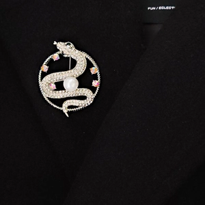 Detail view of a luxury snake brooch with white rhinestones and large pearl on a black suit
