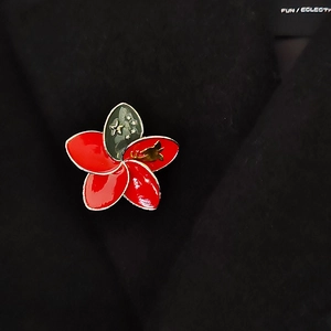 Close-up of a red and green five-petal flower brooch pinned on a black wool blazer lapel