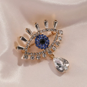 Luxury Evil Eye brooch with blue crystals and a teardrop pendant on champagne silk