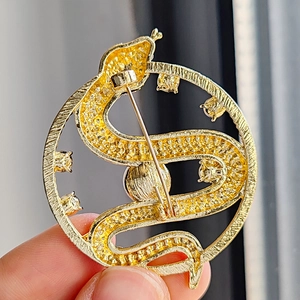 Macro view of a gold snake-shaped brooch featuring scale texture and clear gemstones