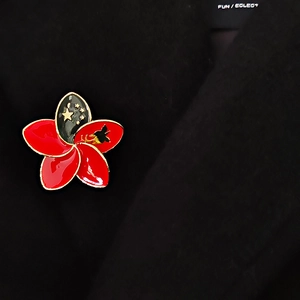 Detail of five-petal flower brooch with enamel red and black petals and golden stars