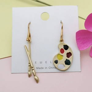 Detalle de pendientes dorados con diseño artístico de pincel y paleta asimétricos