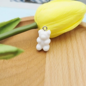 Macro shot of a white resin gummy bear charm with silver loop on a wooden tray