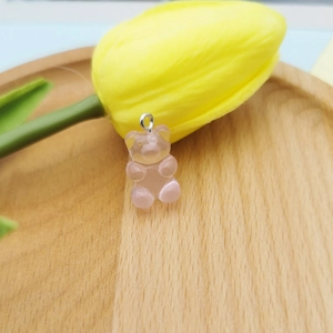 Detailed close-up of a pink resin gummy bear pendant with metal ring on a wooden tray