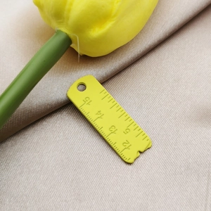 Detail of yellow ruler-shaped alloy pendant with scale markers on champagne satin fabric