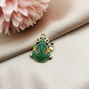 Detail of green enamel frog pendant with gold metal edges on champagne satin fabric
