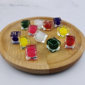 Ciondoli a cubo in resina trasparente con pompon colorati e anelli metallici in un vassoio