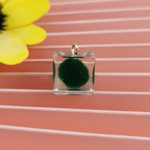 Dettaglio del ciondolo a cubo in resina con palla di muschio verde e anello dorato