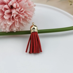 Detail of red faux suede tassel with a gold metal cap hanging for DIY jewelry crafts