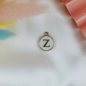 Macro view of gold-plated alloy letter Z charm with white enamel on silk fabric