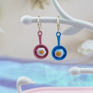 Creative fried egg frying pan earrings in pink and blue on a white jewelry stand