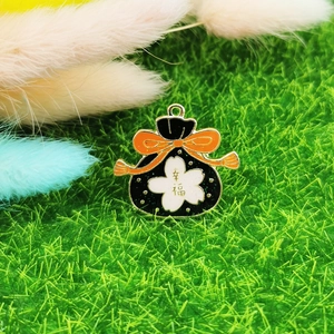 Makro-Detail eines schwarzen Emaille-Glücksbringers mit Kirschblüten und kleiner Metallschlaufe