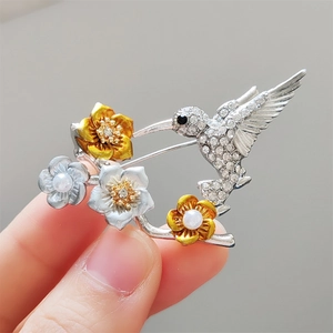 Broche fleur et colibri étincelante avec strass et perles blanches en ton argenté
