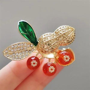 Vue détaillée d'une broche cacahuète avec perles rouges, émail vert et strass
