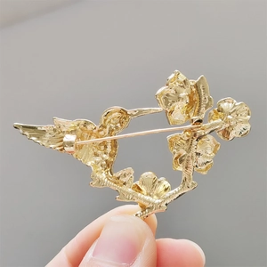 Gros plan détaillé de la broche colibri dorée avec relief floral en métal ciselé