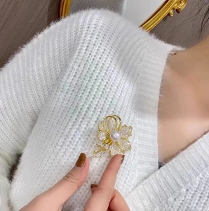 Détail d'une élégante broche fleur dorée avec perles et cristaux sur un tricot blanc