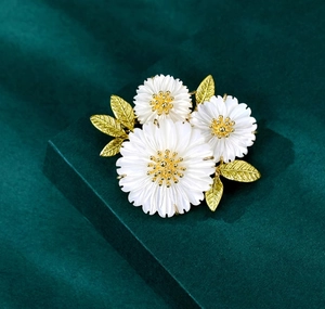 Macro detail of three daisy brooches with white shell petals and gold metallic leaves