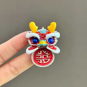 Detail of red Chinese lion dance brooch with enamel finish and a silver joy character pendant