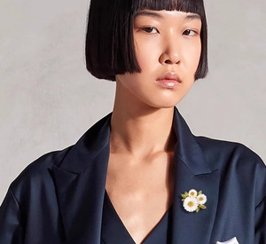 Close-up of white daisy brooch with green enamel leaves on a navy satin blazer lapel