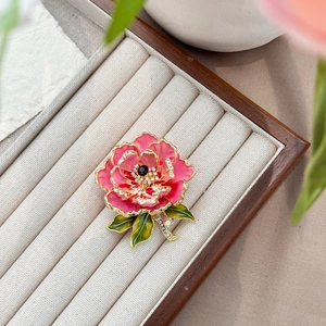 Détail macro d'une broche pivoine émaillée rose avec cristaux sur boîte en bois